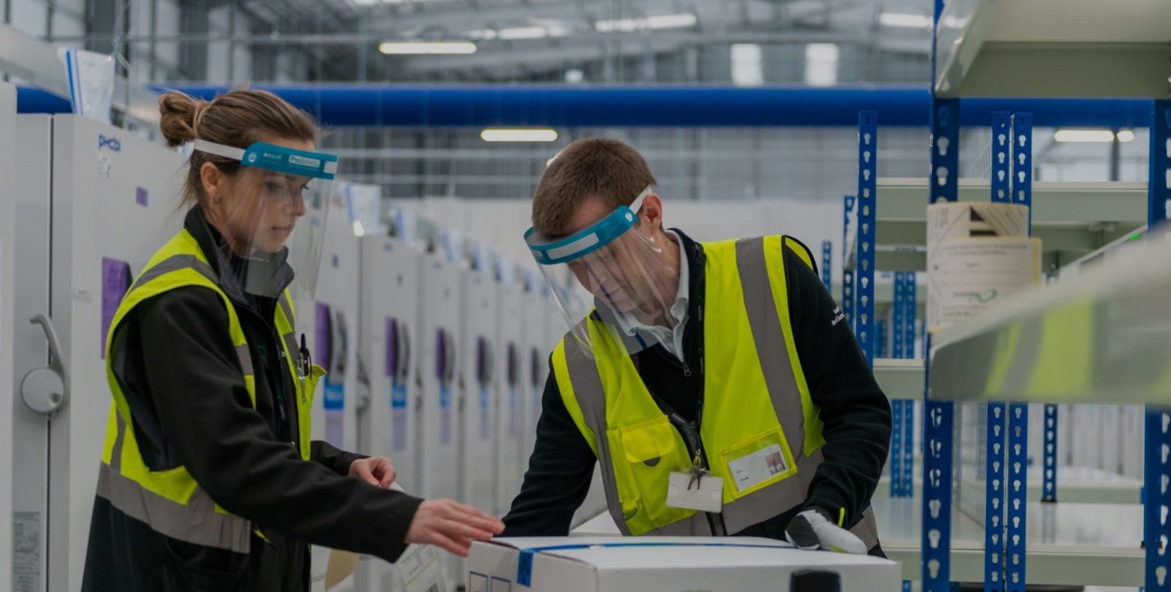 Two employees wearing visors and safety vests collaborating in warehouse