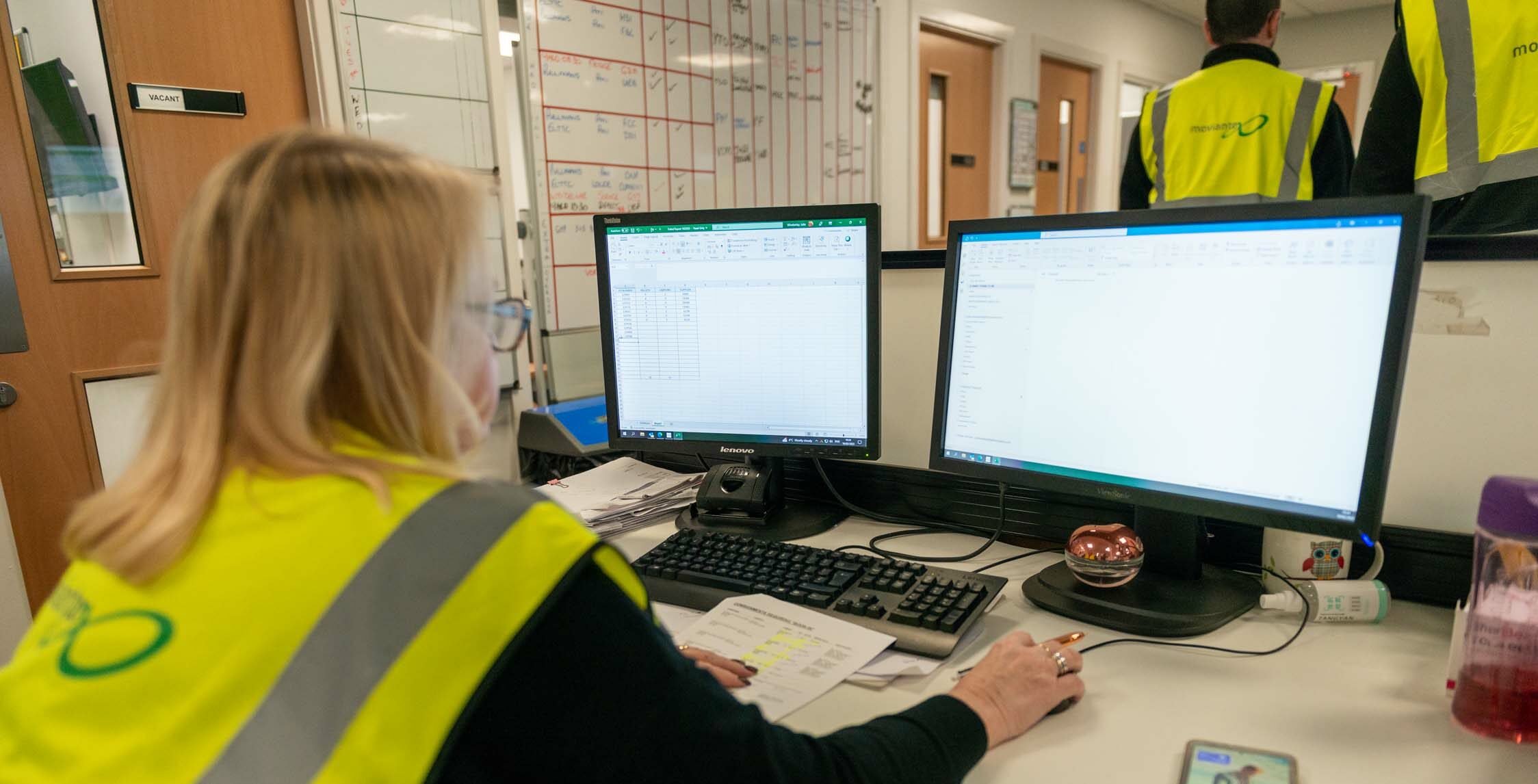 Staff wearing safety vest and working on a computer in an office